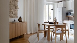 Une cuisine moderne avec des meubles blancs, une table à manger en bois et une grande fenêtre ornée de rideaux légers.