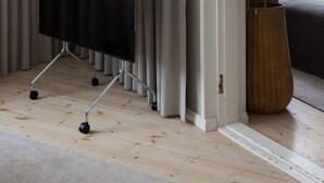 Une pièce avec un grand téléviseur à écran plat noir posé sur un meuble, des rideaux de couleur claire, un panier en osier et un canapé gris.