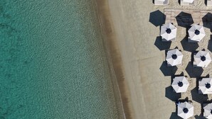 Egy strand légi felvételén fehér napernyők sora és egy fa fedélzet látható.