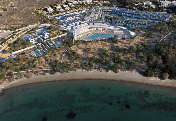 An aerial view of a coastal resort with multiple buildings, a central pool area, and a beach. - Kenshō Paros (Paros)