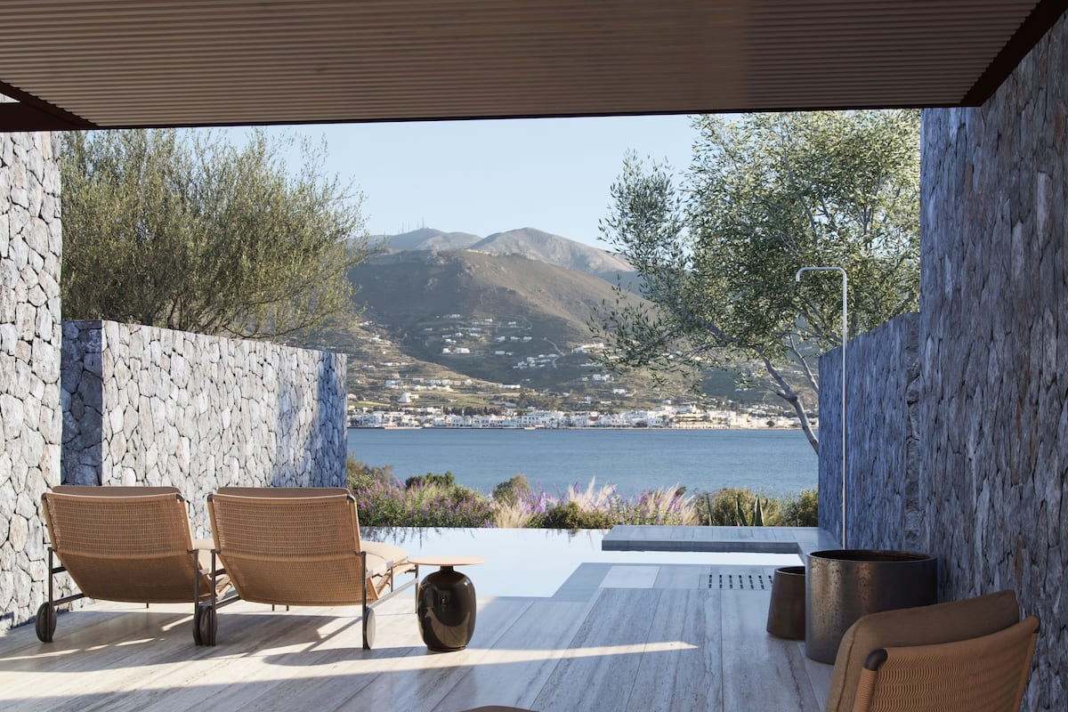 A modern outdoor seating area with wicker chairs and a table, overlooking a scenic view of a lake and mountains.