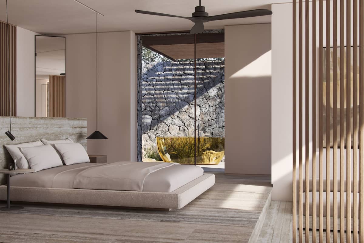A modern bedroom with a large bed, a ceiling fan, a stone wall, and a view of a garden.