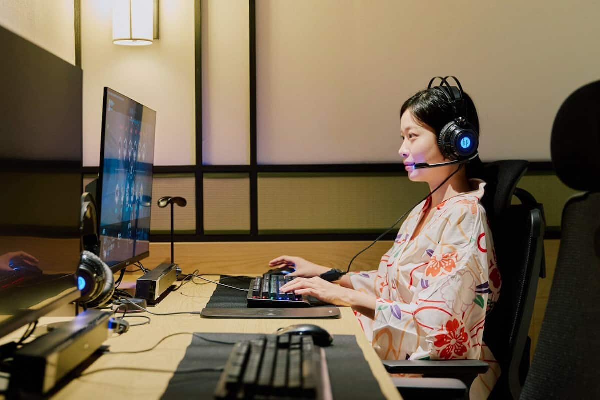 A person using a computer in a room with a large monitor, keyboard, and mouse. There is a headset on the desk.