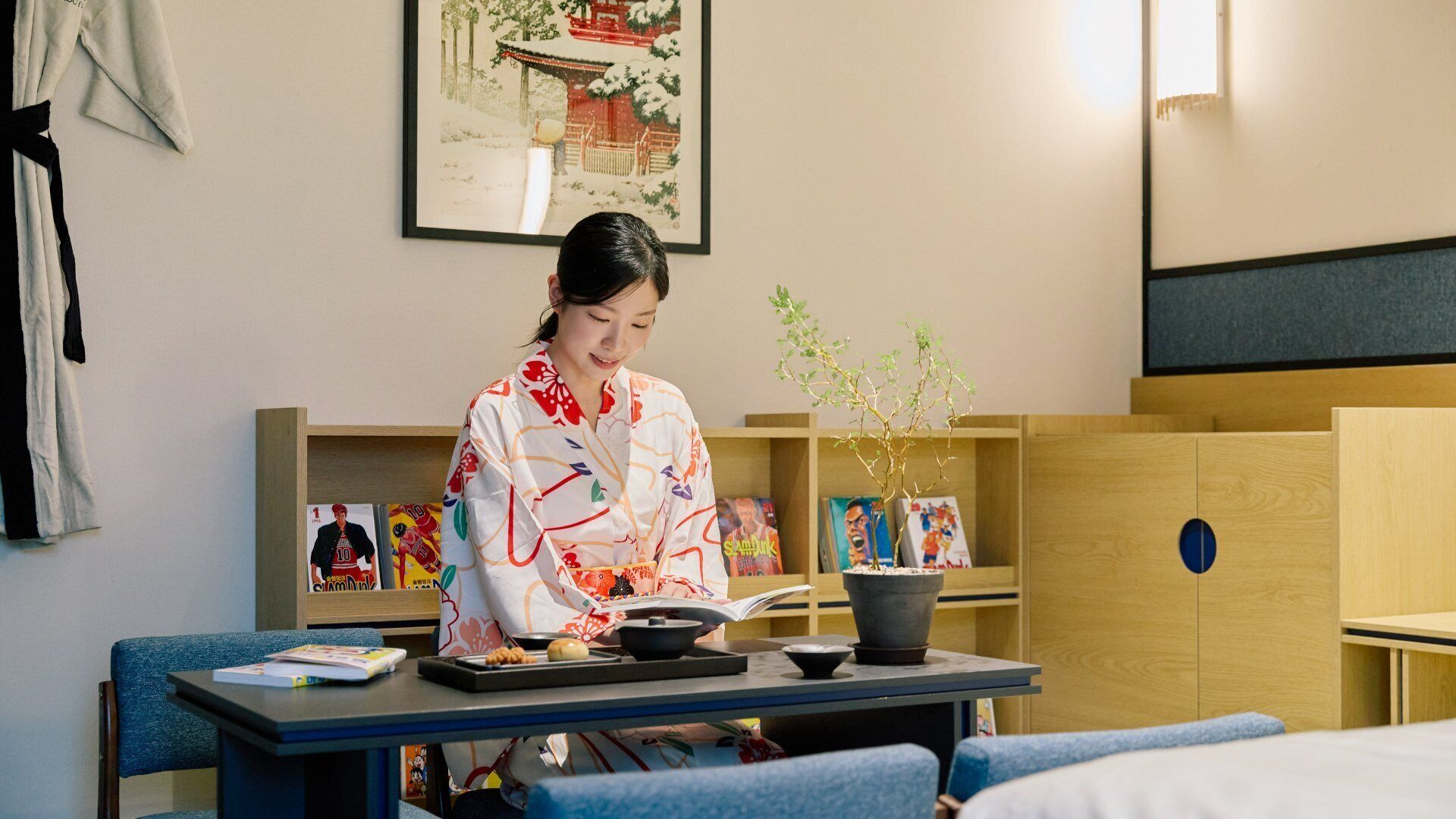 A hotel room with a dining table, a potted plant, and a bookshelf with books and decorative items.