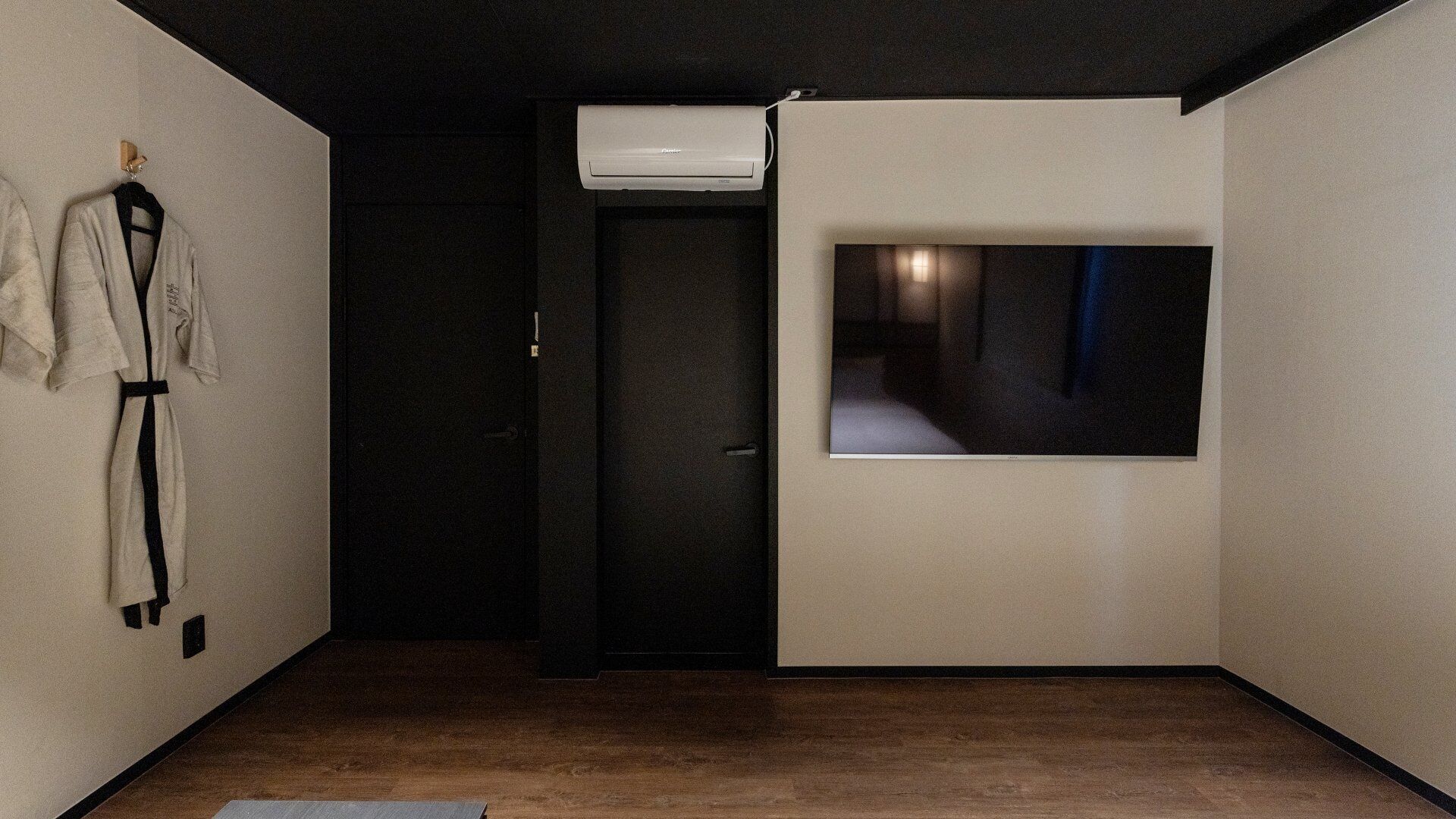 Une pièce avec un plancher en bois, une porte noire et une fenêtre donnant sur un immeuble.