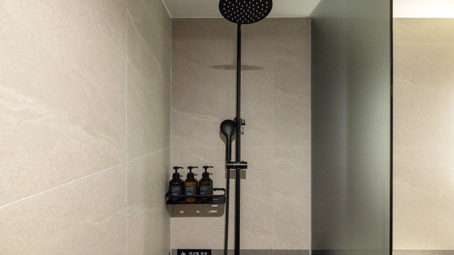 Una ducha moderna con cabezal de ducha manual, dispensador de jabón manual y un dispensador de jabón en un soporte de pared.