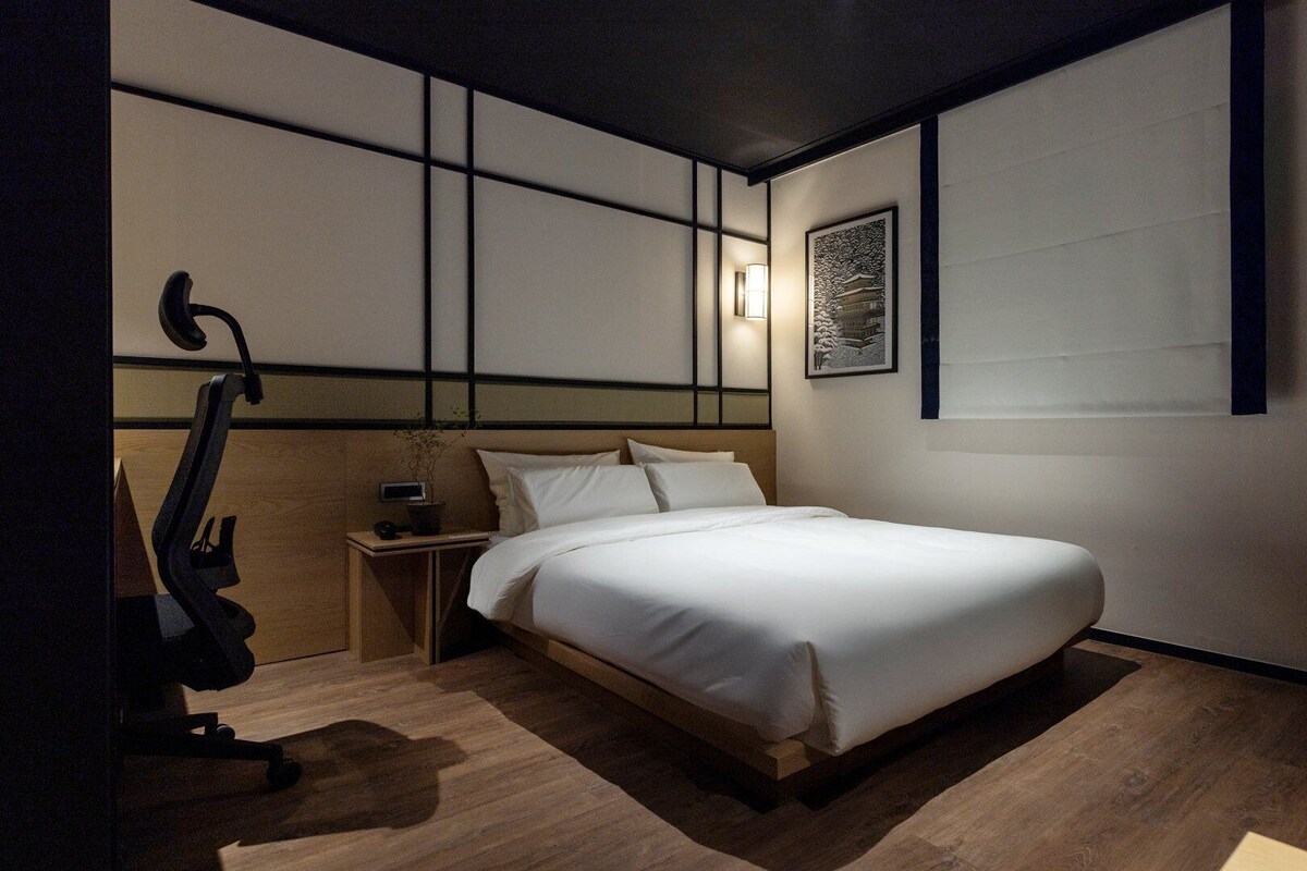 A modern bedroom with a large bed, a nightstand, a desk, and a chair.