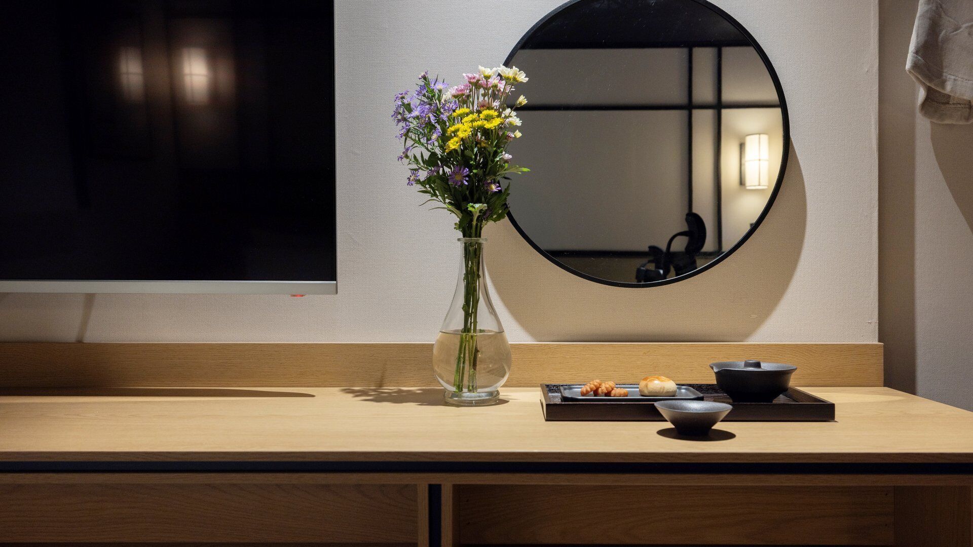A wooden counter with a vase of flowers, a bowl, and a tray of food.