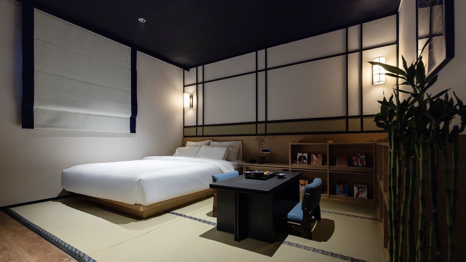 Quarto de hotel moderno com uma cama grande, uma pequena escrivaninha e uma estante.