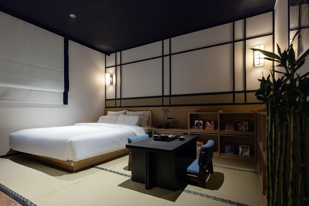 A modern hotel room with a large bed, a small desk, and a bookshelf.