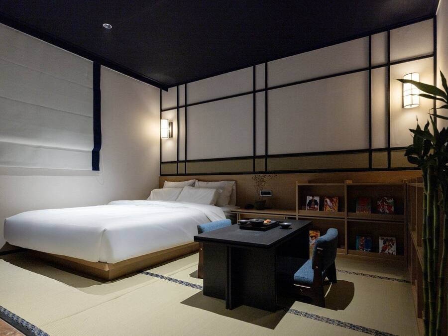 Quarto de hotel moderno com uma cama grande, uma pequena escrivaninha e uma estante.