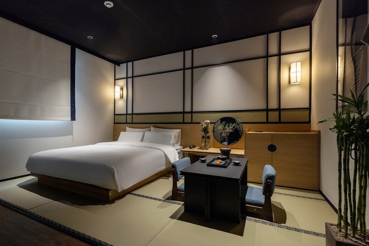 A modern hotel room with a large bed, a small table with a vase, and a mirror.