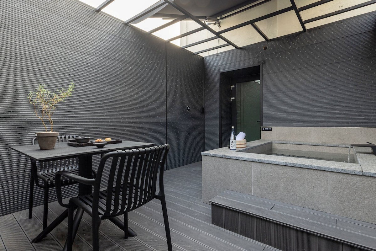 A modern outdoor seating area with a table and chairs, a potted plant, and a hot tub.