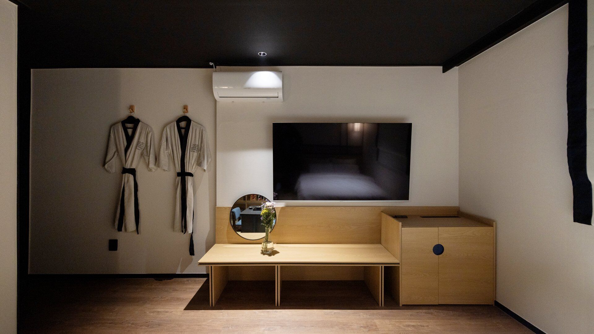 Ein Zimmer mit einem Holztisch, einem an der Wand montierten Fernseher und zwei Wandgarderoben.