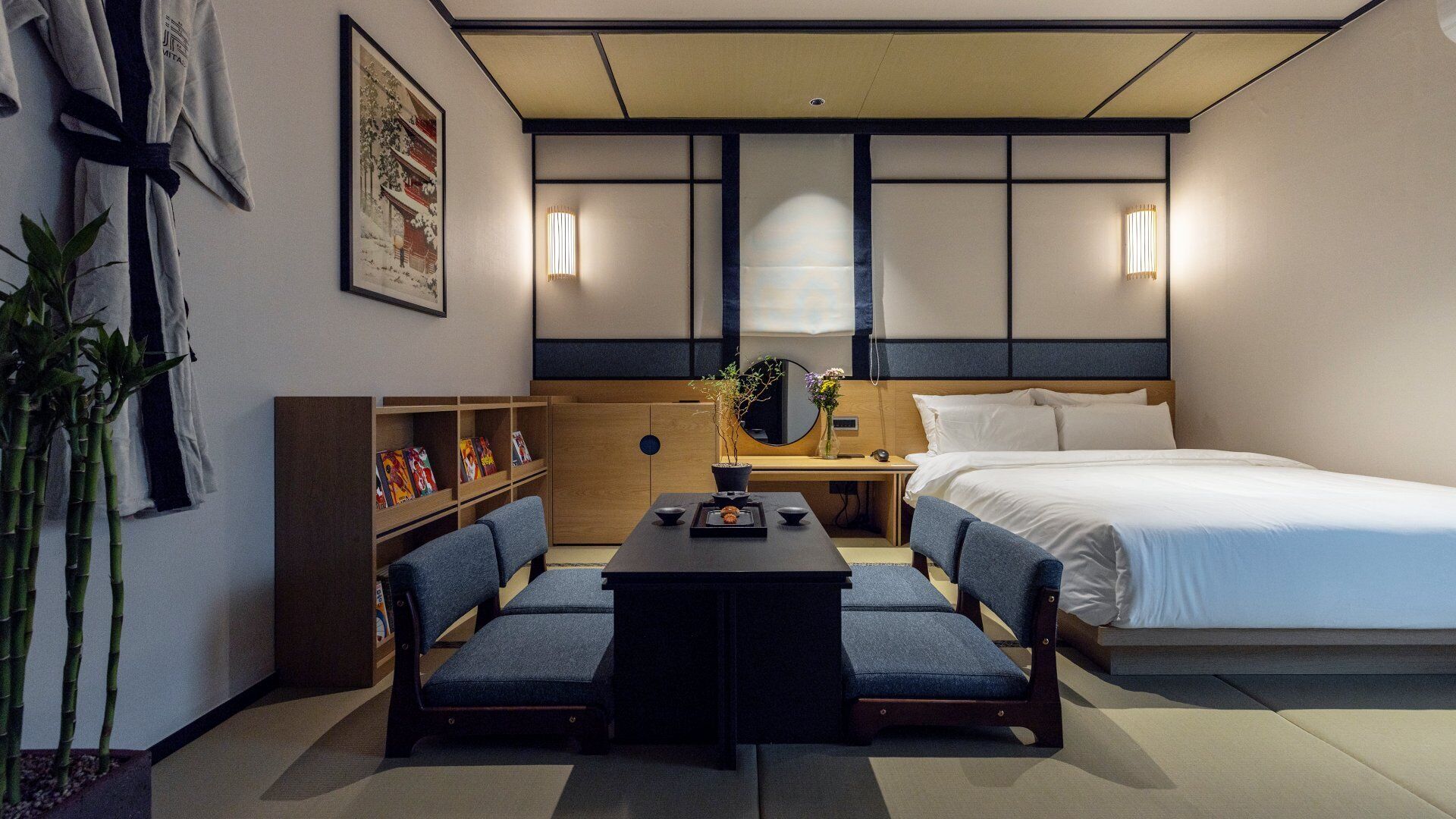 Una habitación de hotel pequeña con cama, escritorio, dos sillas, una estantería y un espejo grande.