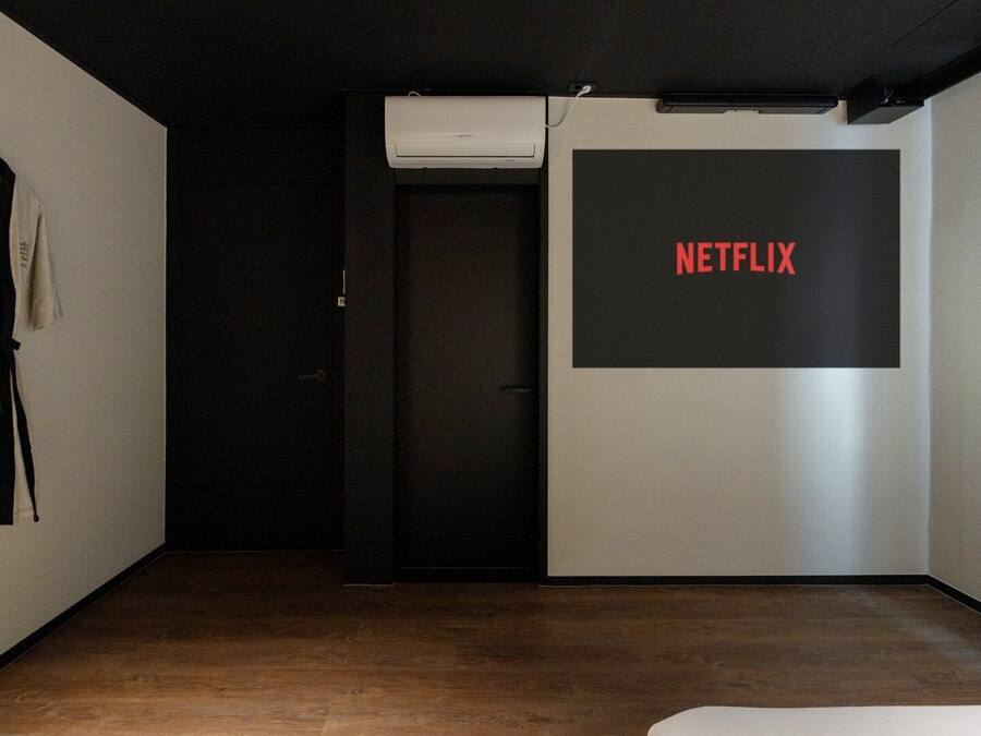 A room with a dark door, a wall-mounted air conditioner, and a large black screen displaying the Netflix logo.