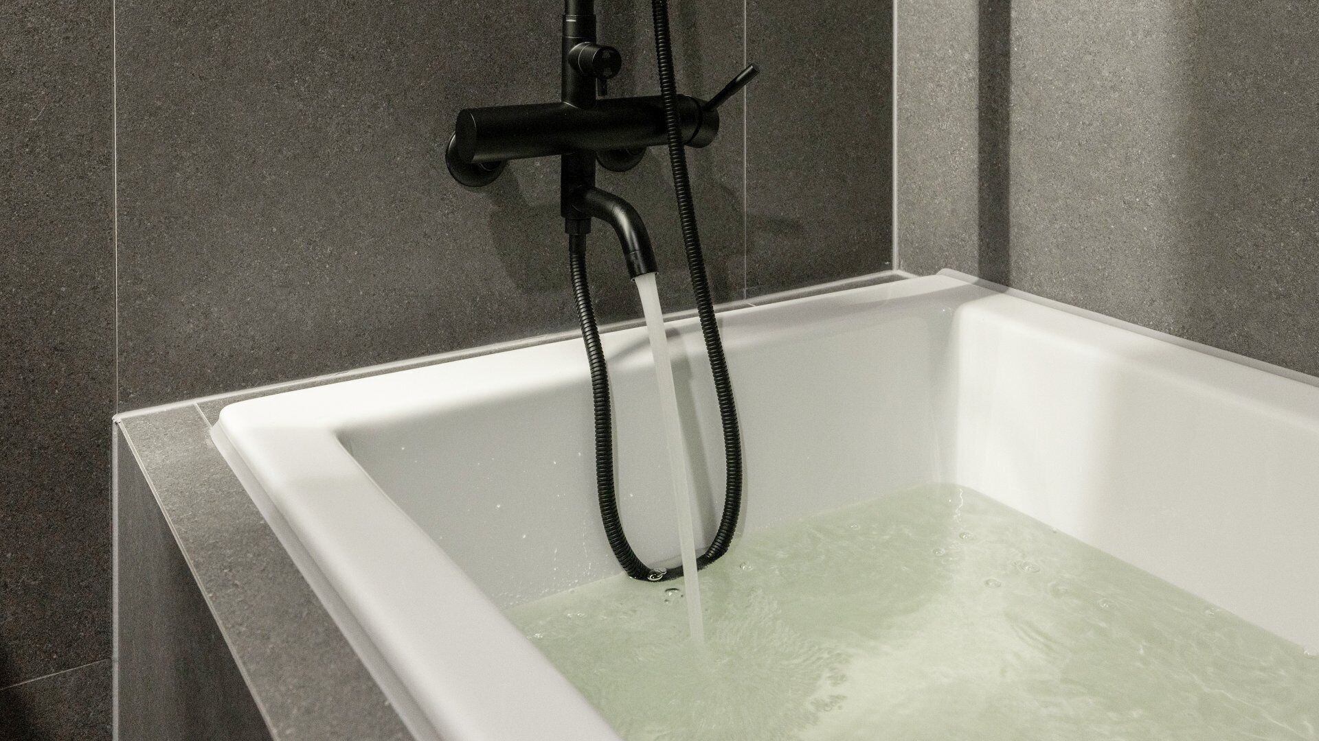 A modern bathtub with a handheld showerhead, set against a tiled wall.