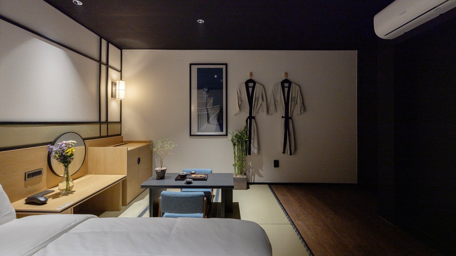 Habitación de hotel con una cama, un escritorio con una computadora, una mesita con una planta y un aire acondicionado de pared.
