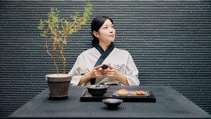 A person seated at a table with a potted plant, a black bowl, and a tray with food items. - Mitasuya Ryokan Hotel by Anook Pyeongtaek Station (Pyeongtaek)