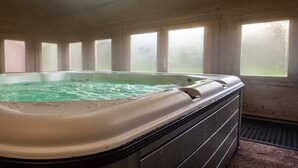 Una bañera de hidromasaje en una habitación con ventanas amplias y techo de madera.
