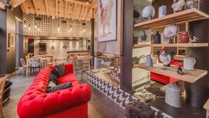 Ein gemütliches Interieur mit einem roten Sofa, Holzbalkendecke und einer Essecke mit Tischen und Stühlen.