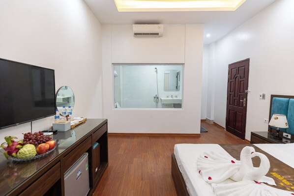 Habitación de hotel con una cama, televisor, escritorio con frutero, espejo y puerta.