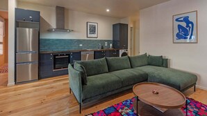 Ein moderner Wohnraum mit einem grünen Sofa, einem Holztisch und einer Küchenzeile mit Edelstahl-Kühlschrank und -Ofen.