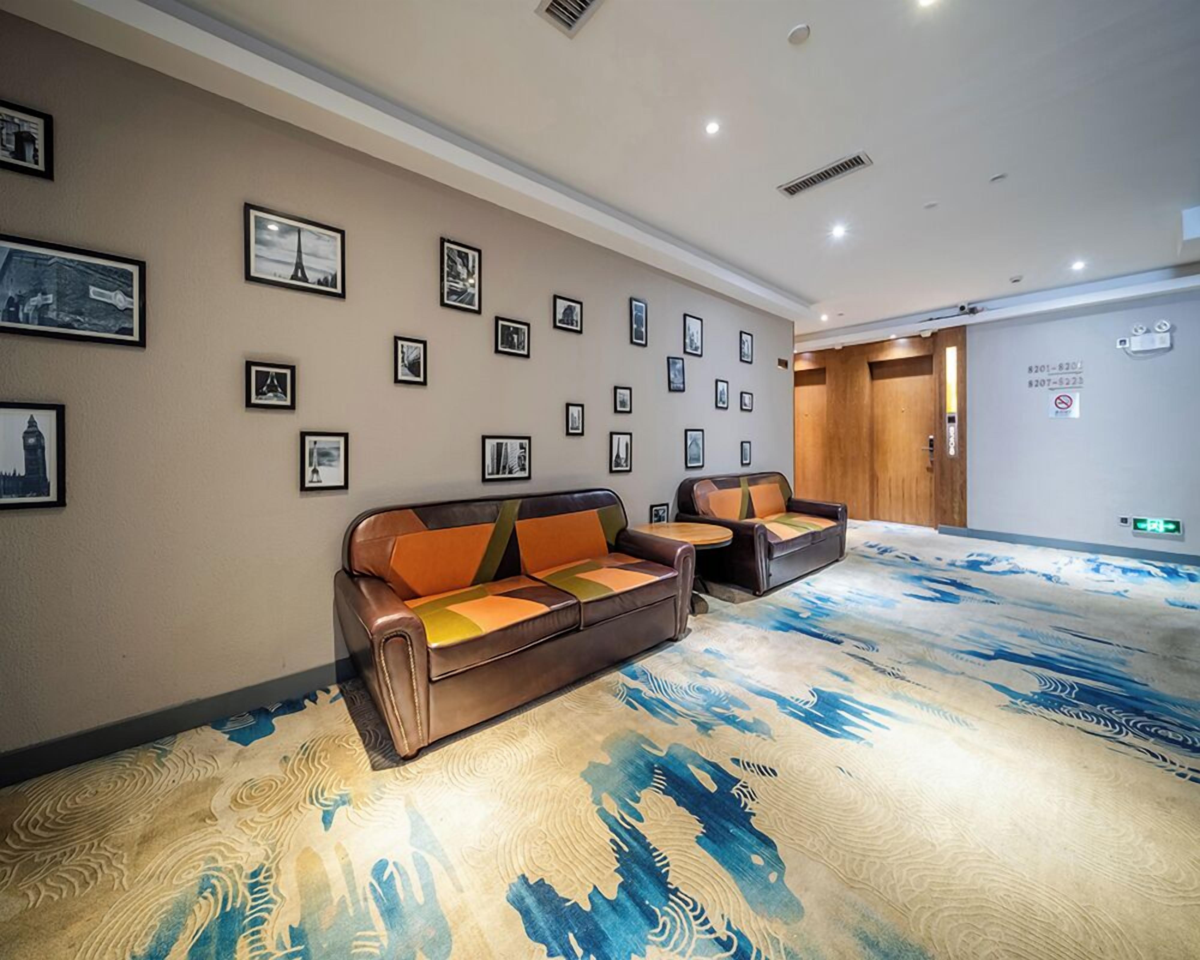 Um saguão de hotel com um tapete grande e estampado, um sofá de couro marrom com almofadas laranja e uma pequena mesa redonda.
