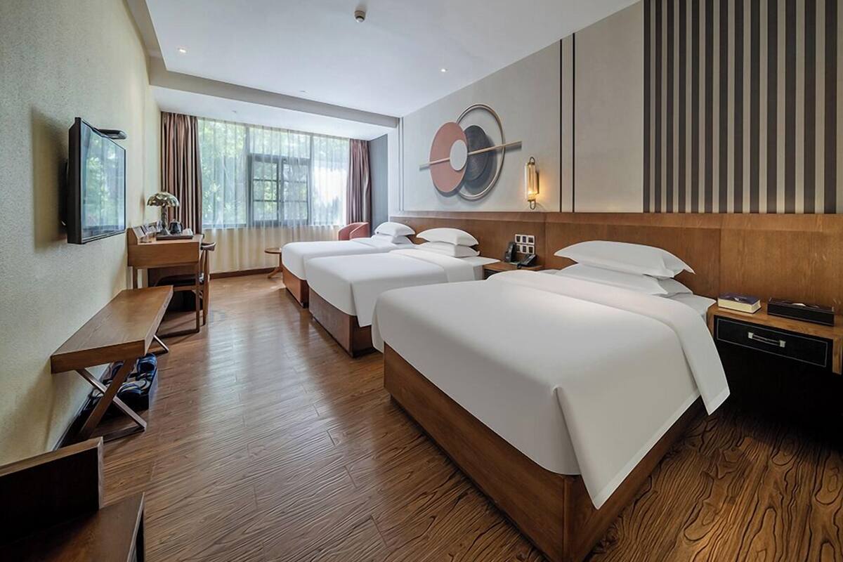 A hotel room with two beds, a desk, a TV, and a large window.