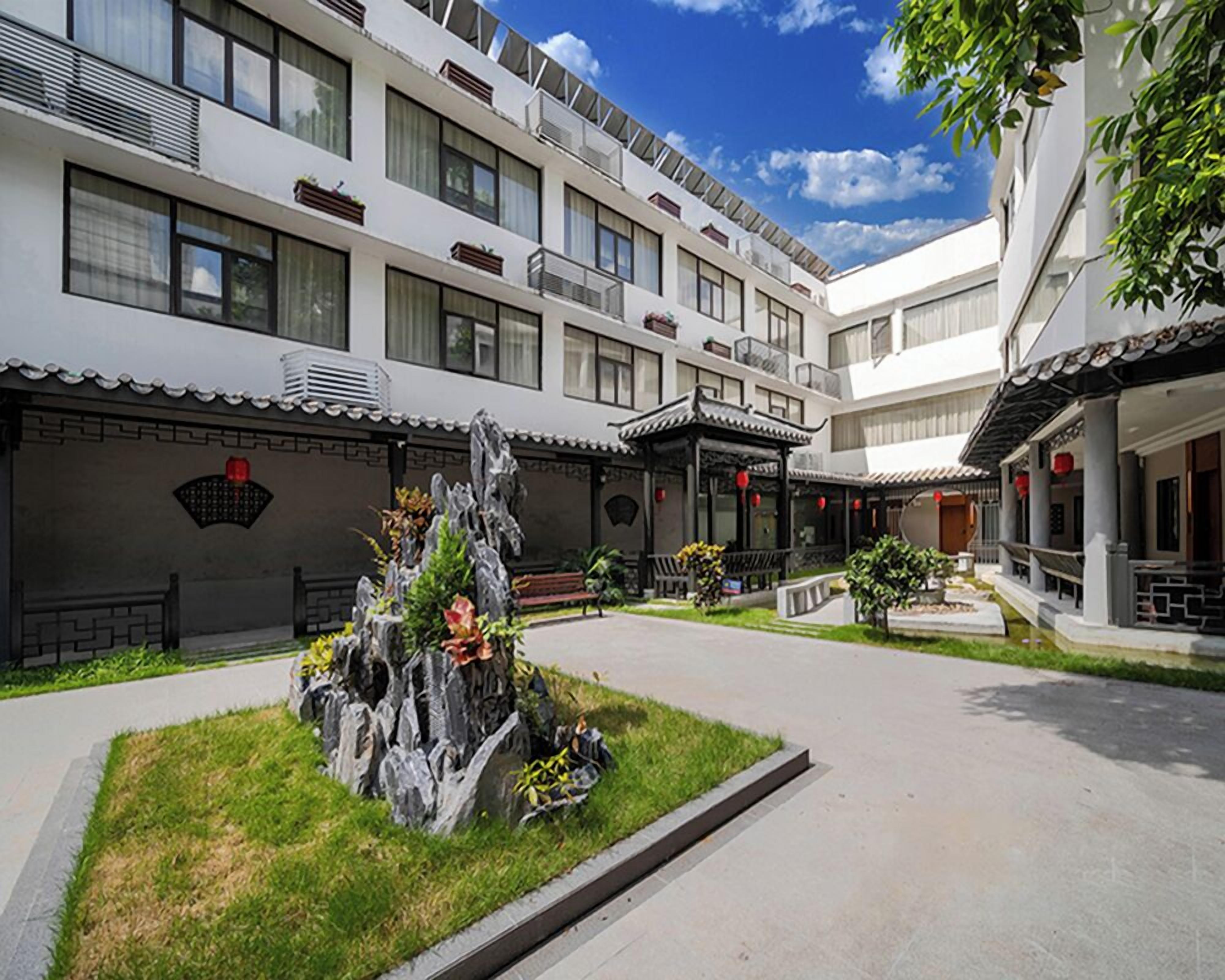 A courtyard with a traditional rock garden, a modern building with balconies, and a traditional pavilion.