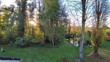 Een tuin met een bankje, bomen en een klein vijvertje.