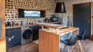 A compact kitchen with a washing machine, a microwave, and a wooden island with chairs. - Le lodge du bassin, Au Calme Absolu (Lindry)