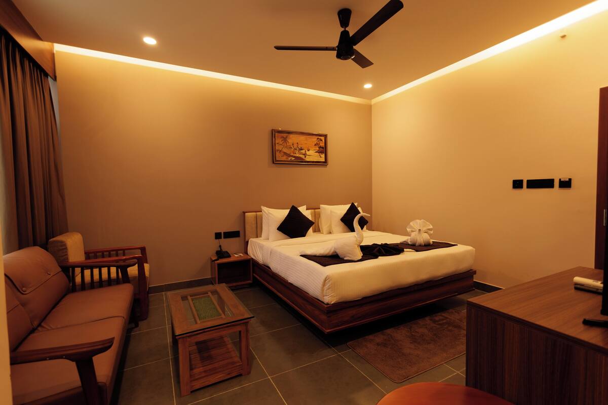 A hotel room with a bed, a sofa, a desk, and a ceiling fan.
