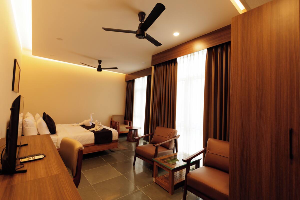 A hotel room with a bed, a desk, a chair, a television, and a ceiling fan.