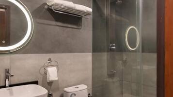 Un baño moderno con ducha envuelta en cristal, inodoro blanco y tocador con espejo.