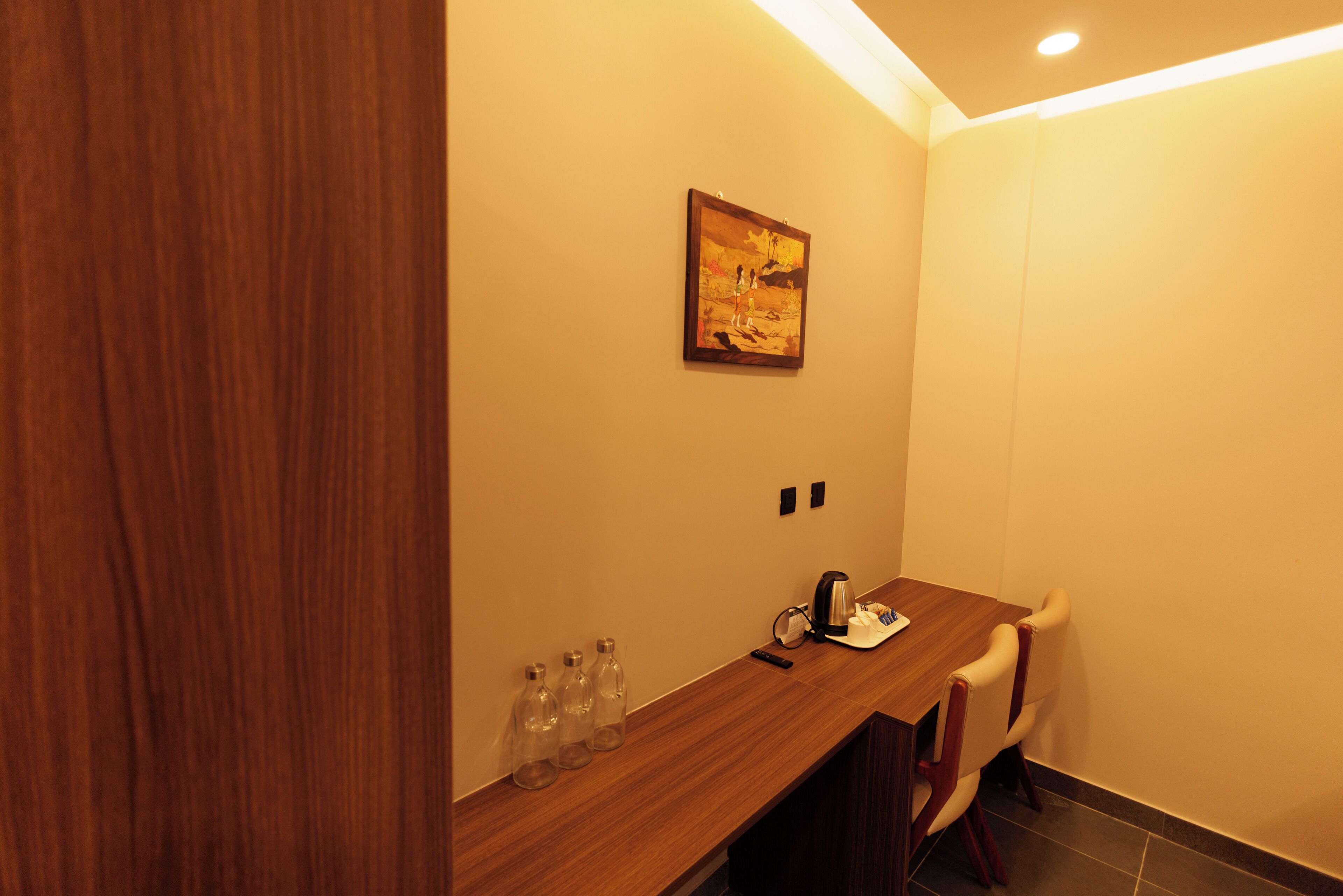 A hotel room with a wooden counter, a painting on the wall, and a chair.