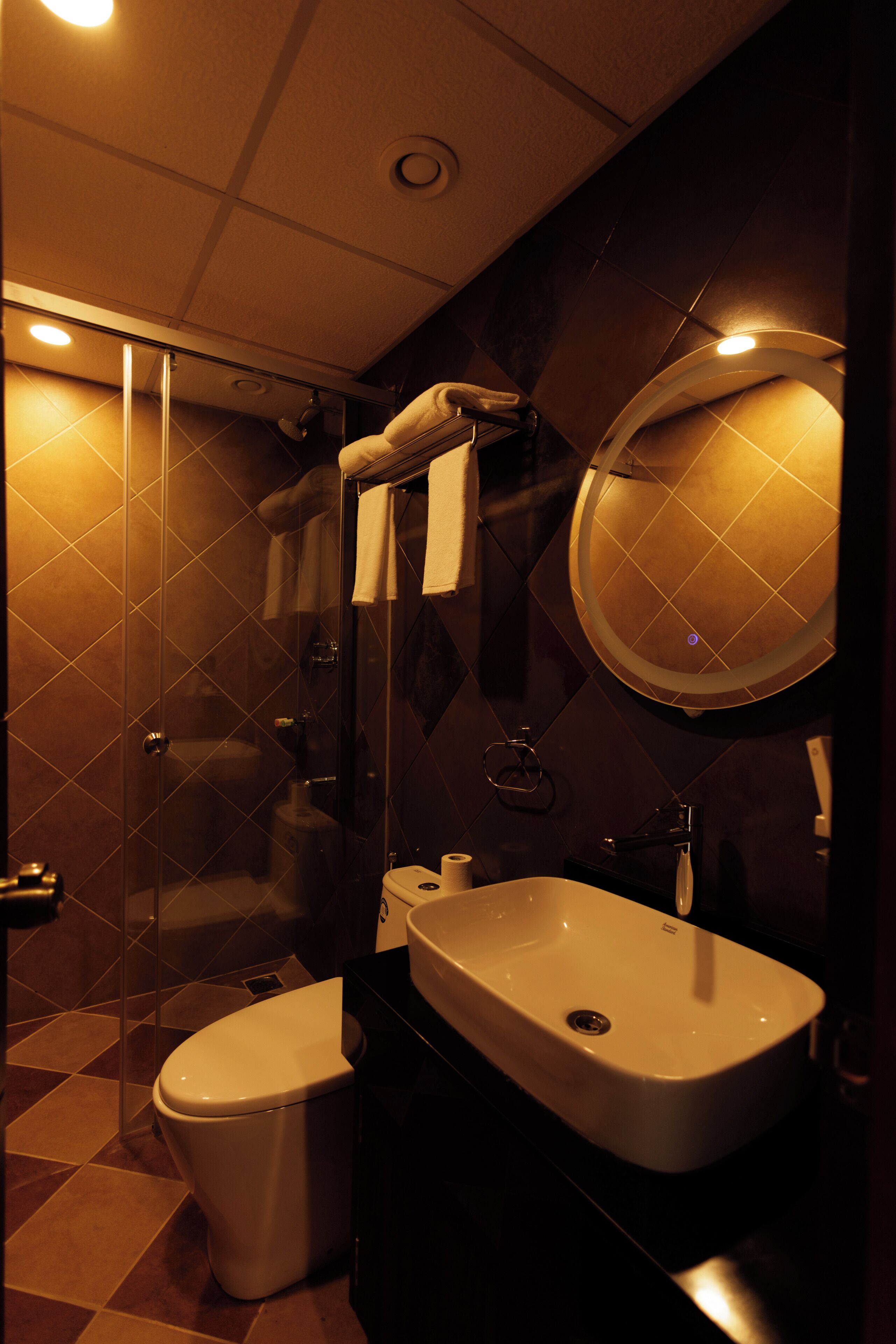 Une salle de bain moderne avec une douche à parois de verre, des toilettes blanches et un lavabo surmonté d’un miroir.