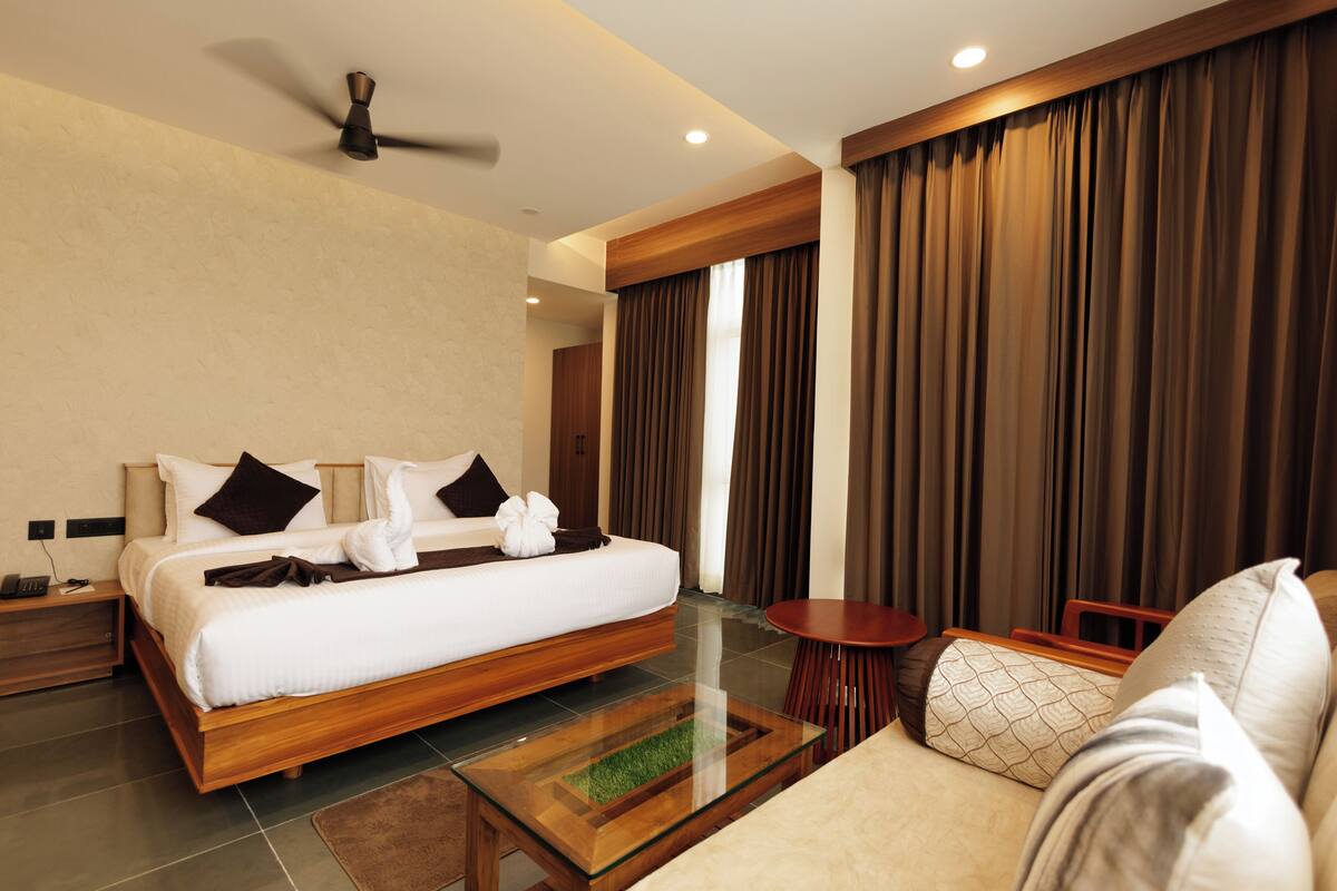 A modern hotel room with a large bed, a sofa, a small table, and a ceiling fan.