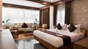 A modern hotel room with a large bed, a sofa, a coffee table, and a desk. - Anasvara Hotels (Mysore)