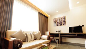A modern living room with a sofa, coffee table, and a flat-screen TV. - Anasvara Hotels (Mysore)