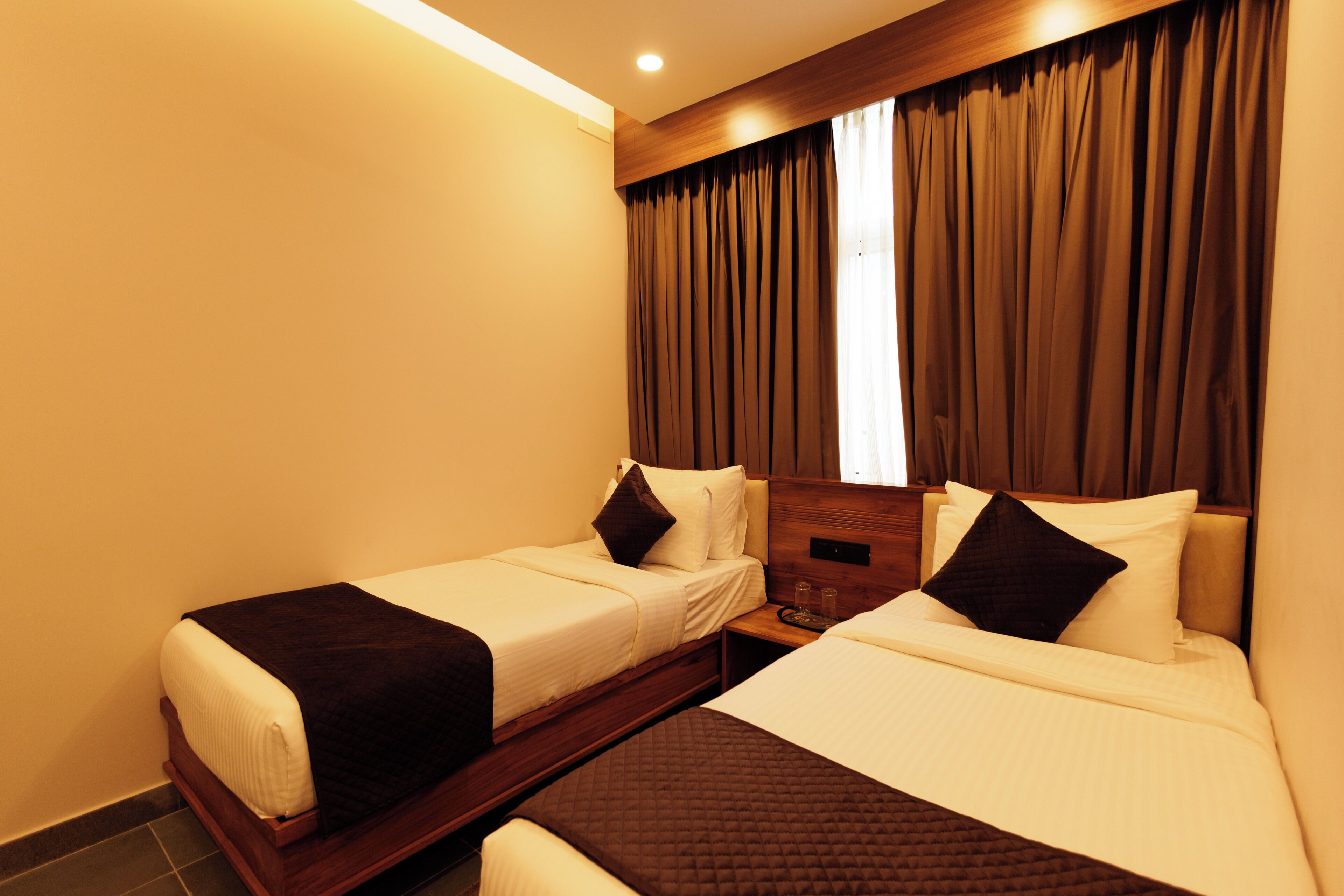 A hotel room with two single beds, a wooden headboard, a nightstand, and a window with curtains.