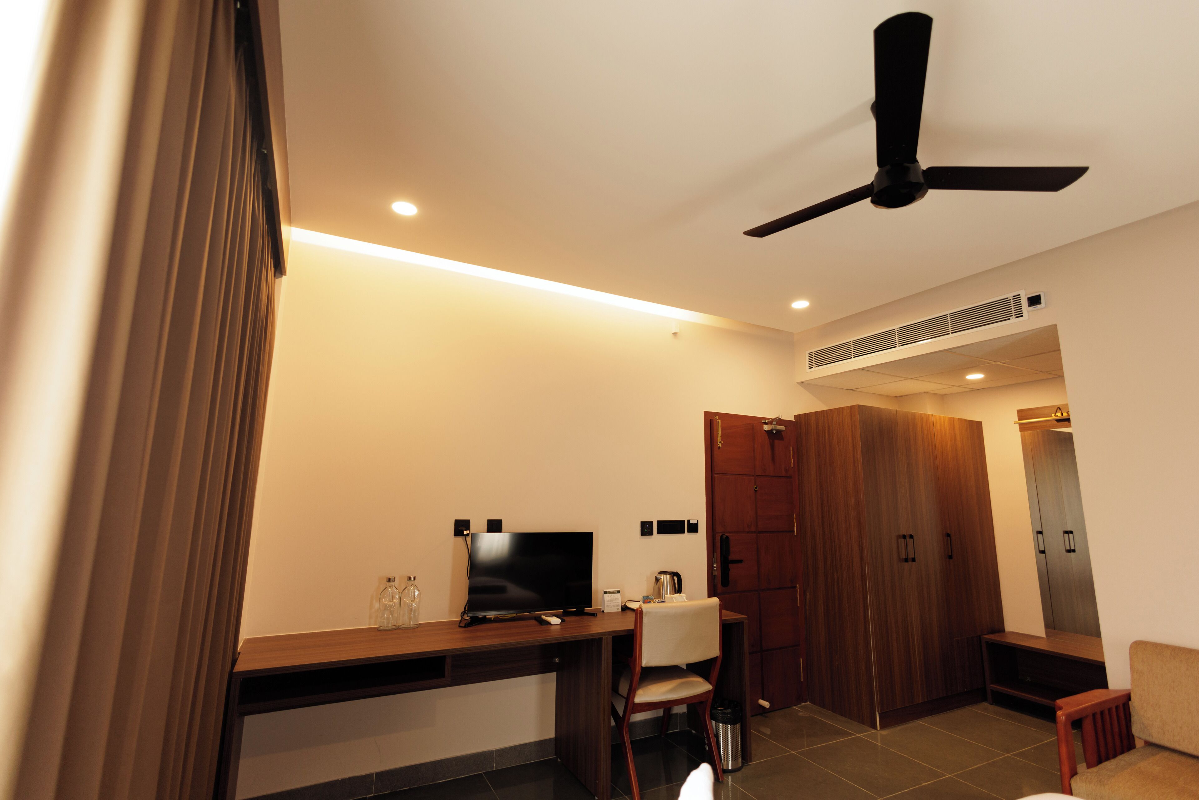 A modern room with a wooden desk, a television, a chair, a ceiling fan, and a wardrobe.