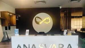 A reception desk with the name 'ANASVARA' and a circular logo above it. - Anasvara Hotels (Mysore)