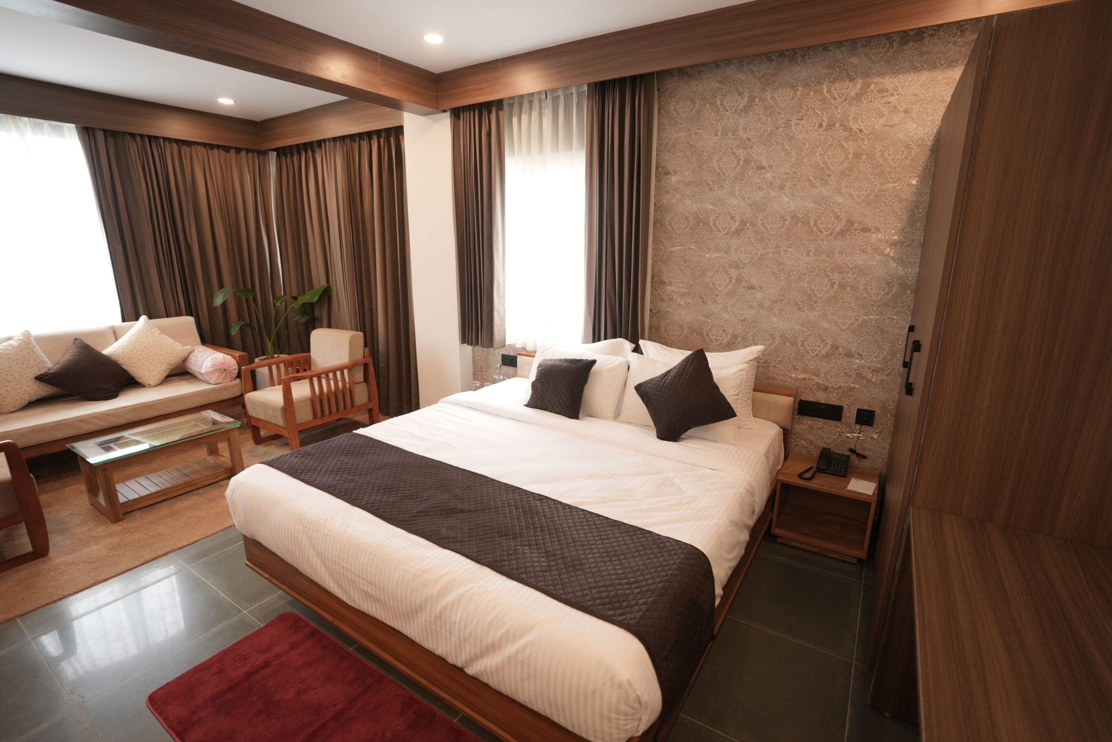 A modern hotel room with a large bed, a sofa, a small table, and a nightstand with a phone.