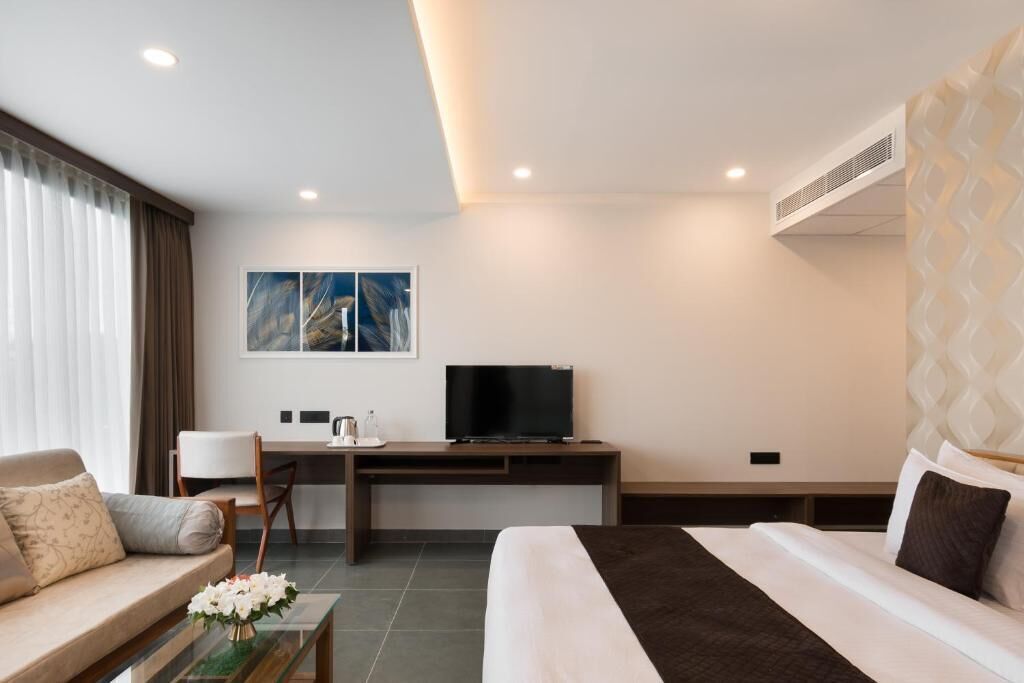 A hotel room with a bed, a sofa, a desk with a TV, and a painting on the wall.