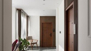 A modern hallway with a wooden door, a chair, and potted plants. - Anasvara Hotels (Mysore)