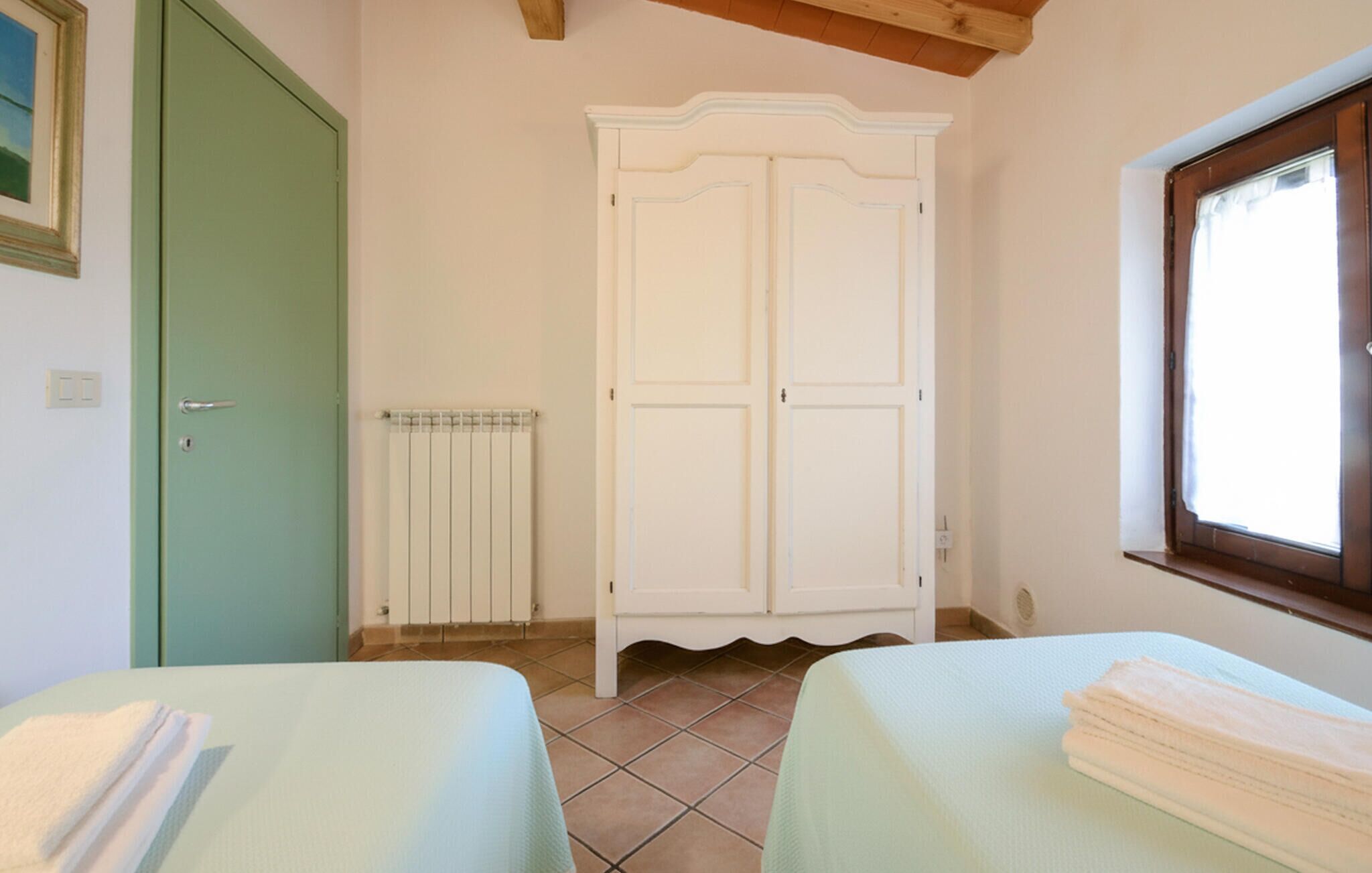Une chambre avec deux lits, un radiateur, une porte verte et une fenêtre avec des rideaux.