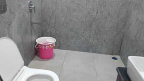 A bathroom with a toilet, a pink bucket, and a bathtub. - Anand Vihar Hotel (Ambajipeta)