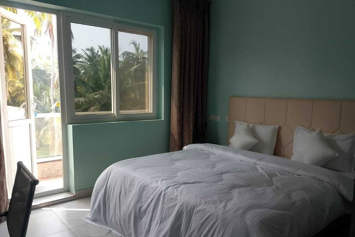 A bedroom with a bed, a window, and a view of palm trees.