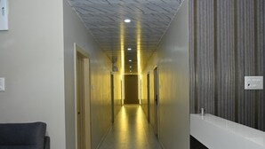 A hallway with doors on both sides, a reception desk, and a chair. - Anand Vihar Hotel (Ambajipeta)
